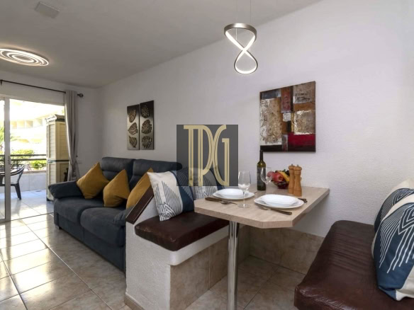 Open-plan living area with a dark blue sofa and mustard cushions, adjacent to a small dining nook set for two.
