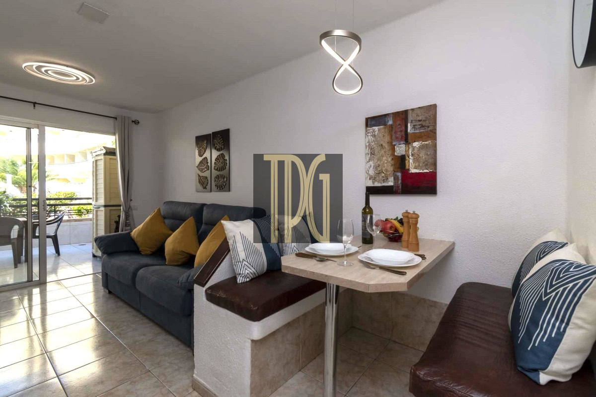 Open-plan living area with a dark blue sofa and mustard cushions, adjacent to a small dining nook set for two.