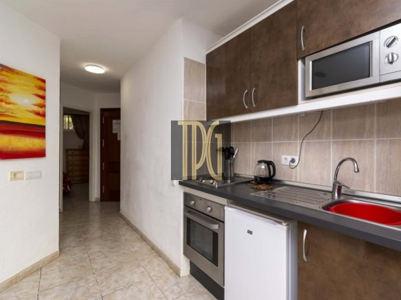 Compact kitchen with brown upper cabinets, stainless steel oven and microwave, red sink, and small white fridge beside the counter.