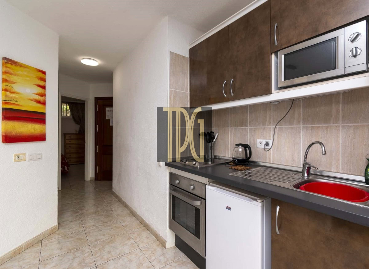 Compact kitchen with brown upper cabinets, stainless steel oven and microwave, red sink, and small white fridge beside the counter.