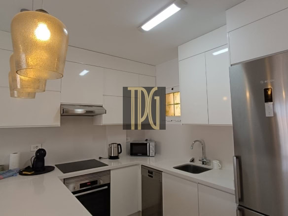 Modern white kitchen with stainless fridge, oven, microwave, and sink under bright pendant lights