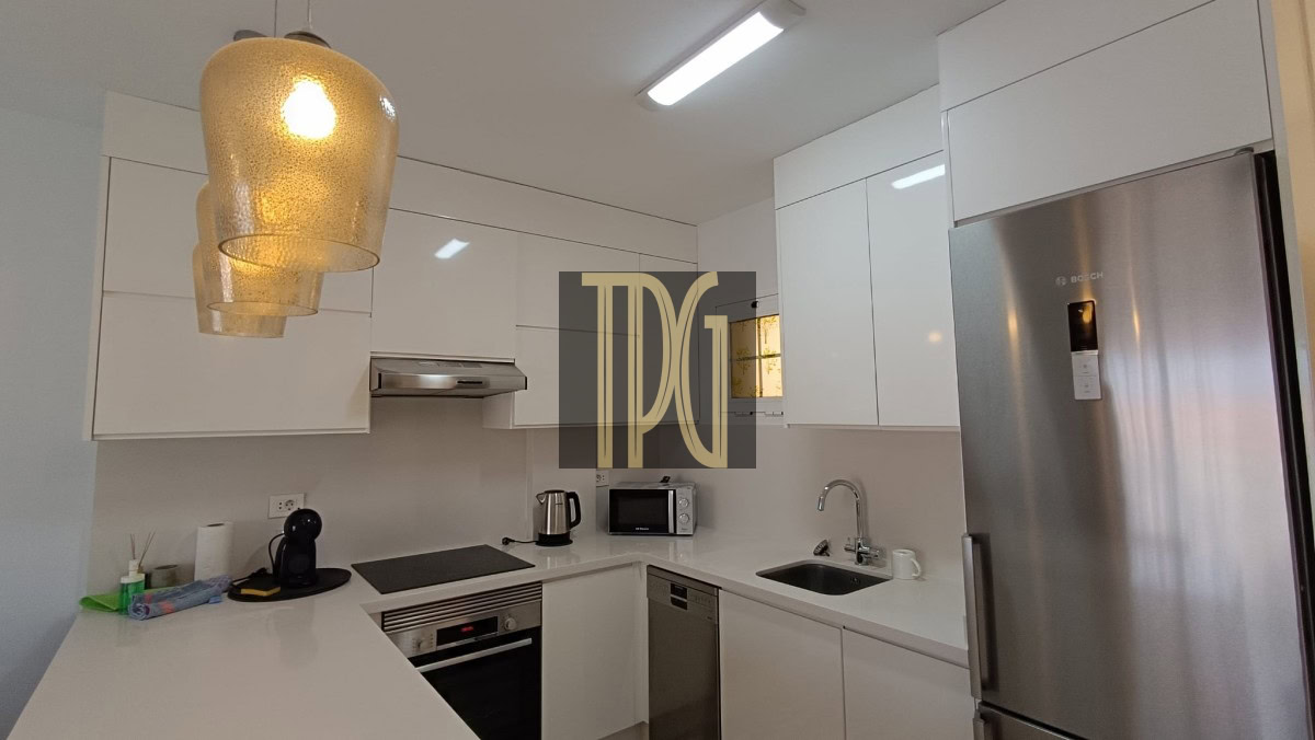 Modern white kitchen with stainless fridge, oven, microwave, and sink under bright pendant lights