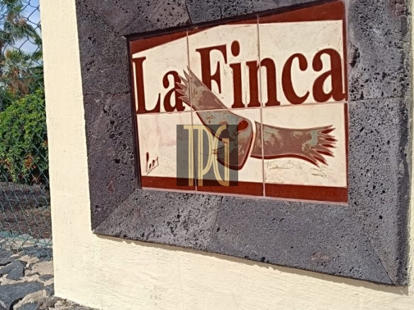 Wall-mounted tile sign reading 'La Finca' with a bird illustration, set in a dark stone frame above a rock base.