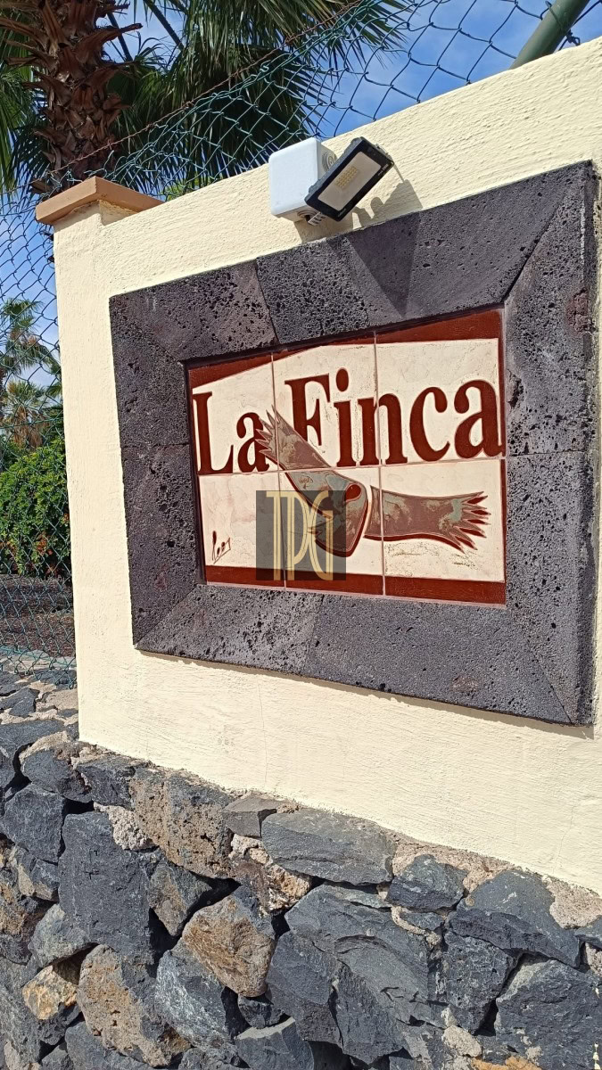 Wall-mounted tile sign reading 'La Finca' with a bird illustration, set in a dark stone frame above a rock base.