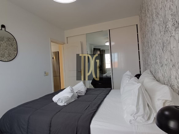 Double bed with white sheets and a dark gray quilt, two rolled towels, an oval mirror, and a sliding closet.