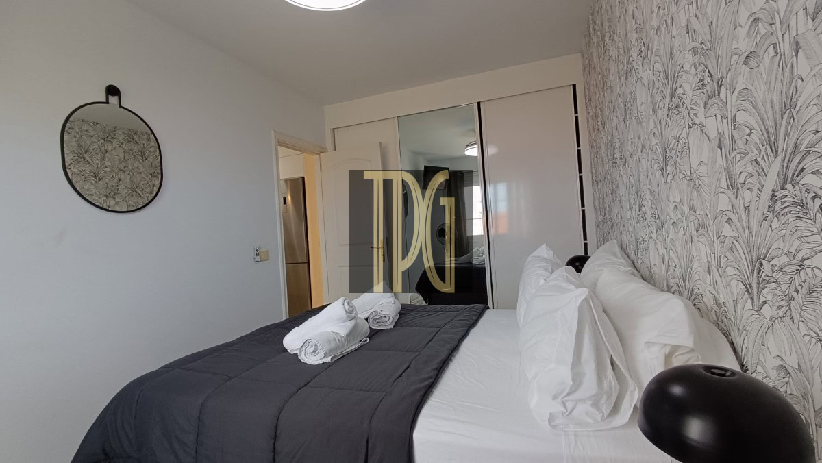 Double bed with white sheets and a dark gray quilt, two rolled towels, an oval mirror, and a sliding closet.