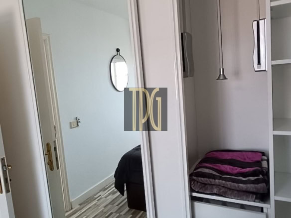 Bedroom wardrobe with full-length mirrored sliding doors; open shelves and folded towels inside reflect the adjacent bedroom in the mirror.
