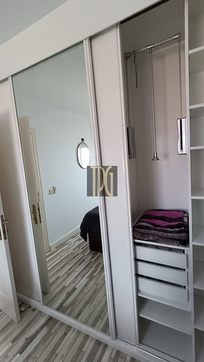 Bedroom wardrobe with full-length mirrored sliding doors; open shelves and folded towels inside reflect the adjacent bedroom in the mirror.