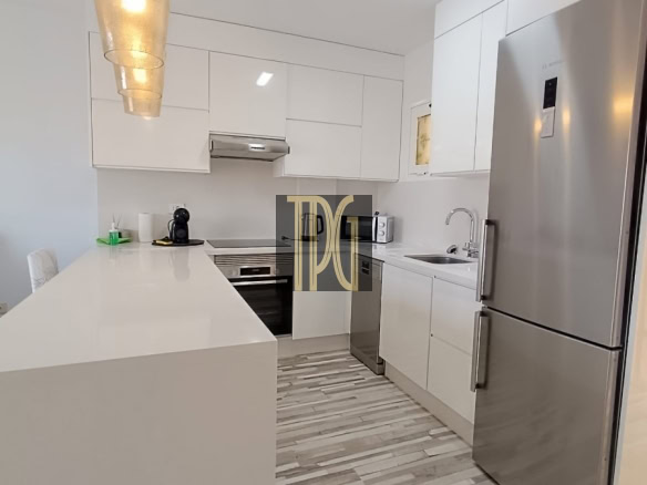 Modern white kitchen with an island, stainless steel fridge and built‑in oven.
