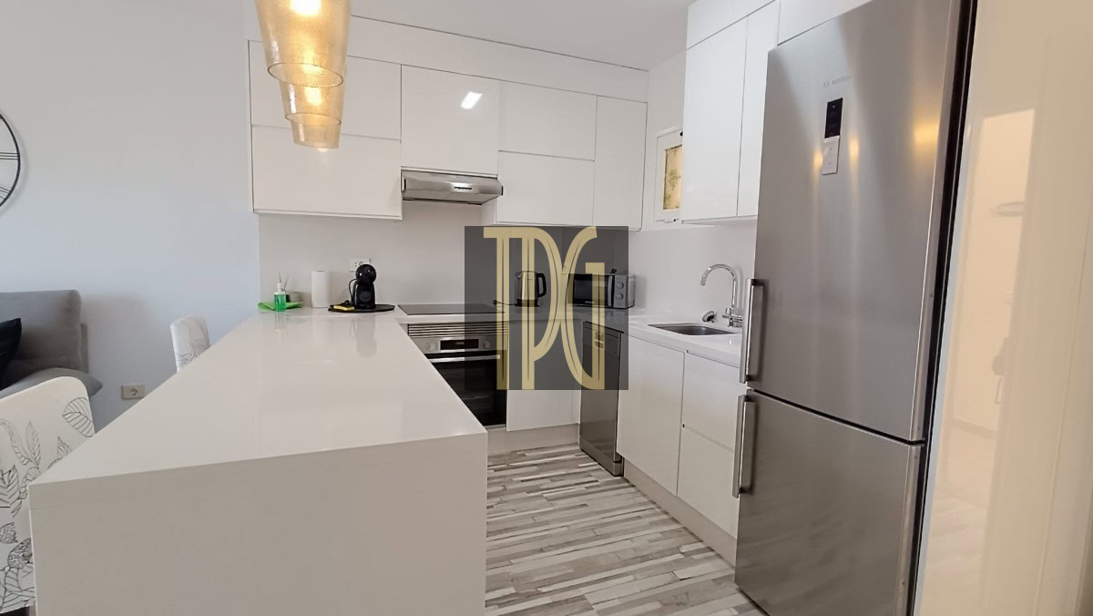 Modern white kitchen with an island, stainless steel fridge and built‑in oven.