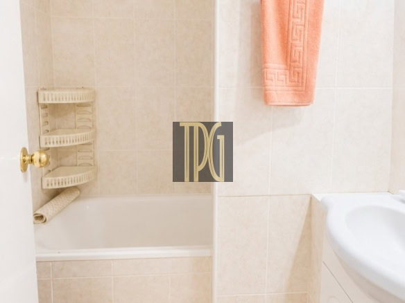 Compact beige-tiled bathroom with a bathtub, peach towel on a chrome rack, and a white vanity on the right.”
