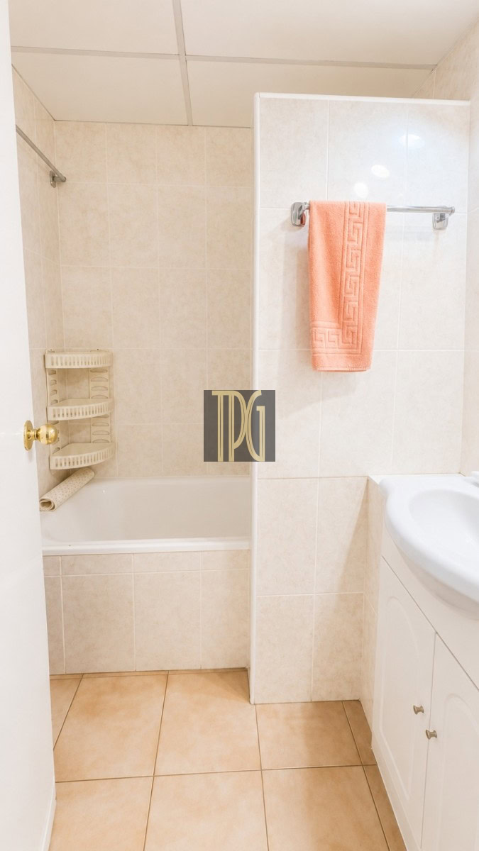Compact beige-tiled bathroom with a bathtub, peach towel on a chrome rack, and a white vanity on the right.”