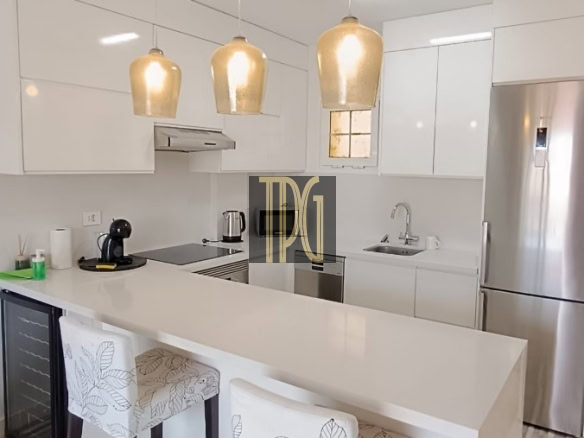 Bright white modern kitchen with an island, three pendant lights, and bar stools with leaf-pattern upholstery in a clean, minimalist space.