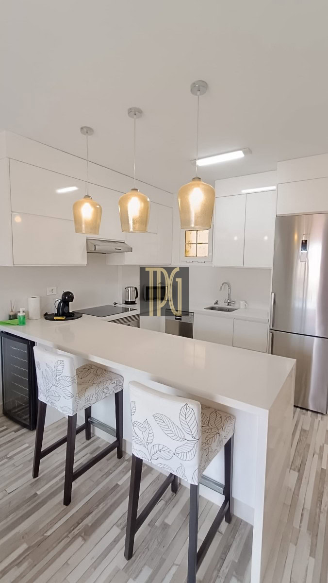 Bright white modern kitchen with an island, three pendant lights, and bar stools with leaf-pattern upholstery in a clean, minimalist space.