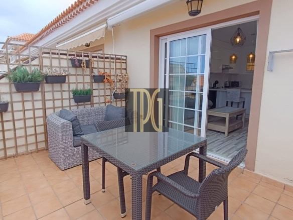 Terrace with wicker dining set and glass table, potted plants on a wooden trellis wall, sliding door to indoors.