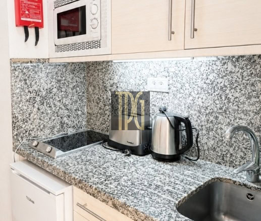 Compact kitchen with granite counters, white cabinets, stove, microwave, and a kettle on the counter; a red fire extinguisher is mounted on the wall.
