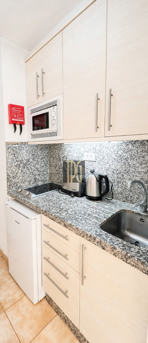 Compact kitchen with granite counters, white cabinets, stove, microwave, and a kettle on the counter; a red fire extinguisher is mounted on the wall.