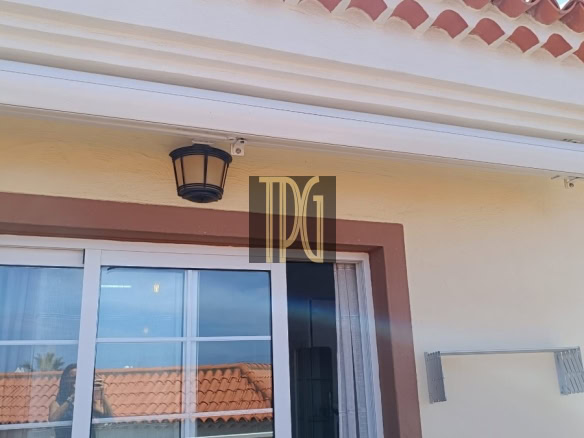 White retractable awning over a glass door on a beige stucco wall with brown trim and a black lantern-style light above.