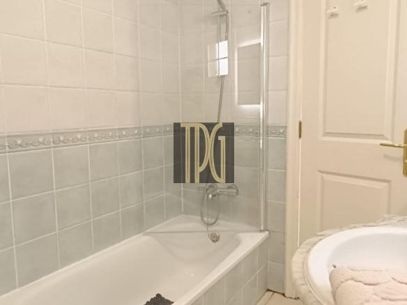 Bathroom with a white bathtub and shower, glass shower screen, tiled walls, and a sink with a towel on the right.
