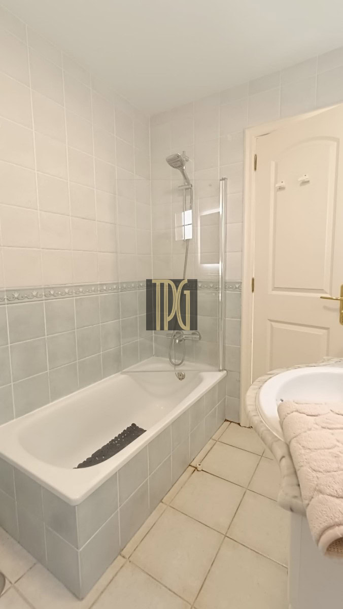 Bathroom with a white bathtub and shower, glass shower screen, tiled walls, and a sink with a towel on the right.