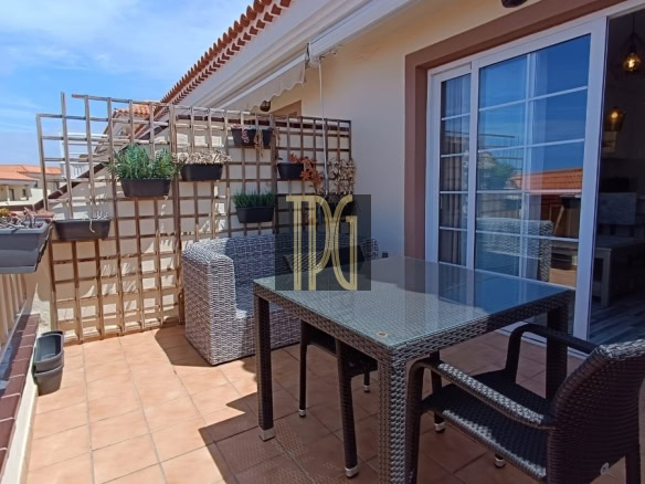 Outdoor balcony with a glass-top wicker table and chairs, potted plants on a trellis against a sliding door. I"m the text