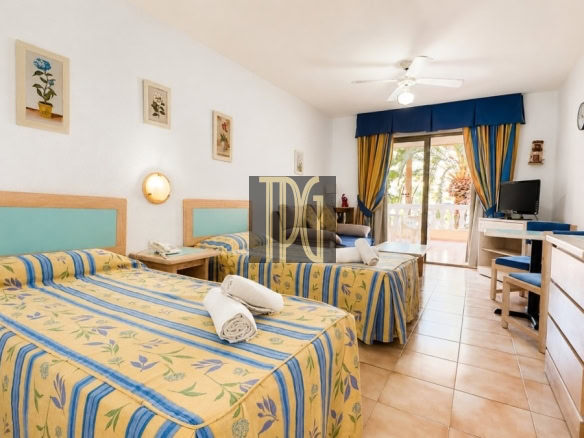 Twin-bed hotel room with yellow-blue floral bedspreads and turquoise headboards; towels on beds and a balcony door with blue curtains in background.