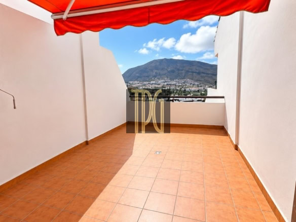 Terracotta-tiled rooftop terrace with a red awning and a mountain view behind white walls.