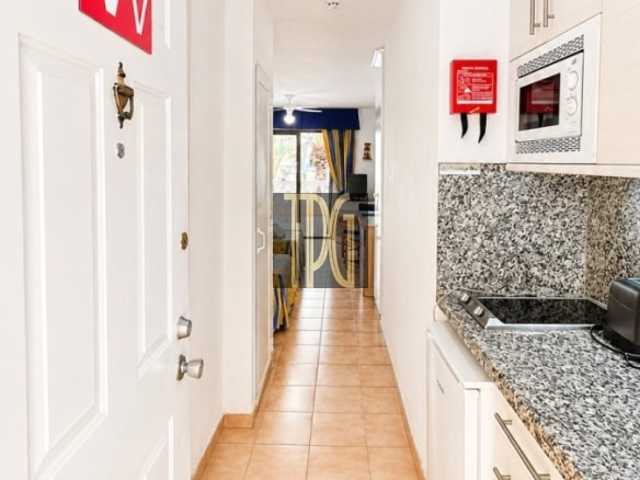 Narrow kitchen hallway with white cabinets and granite countertop, leading to a living area in the distance.