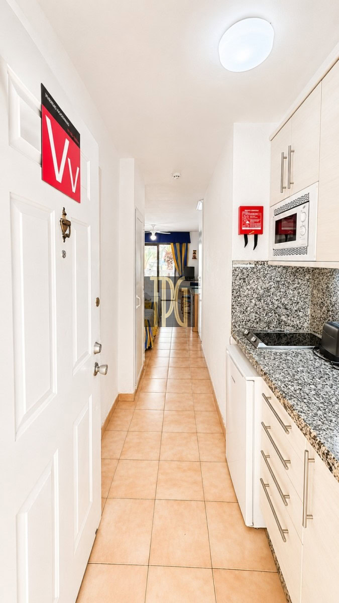 Narrow kitchen hallway with white cabinets and granite countertop, leading to a living area in the distance.