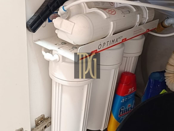 Under-sink water filtration system with reverse osmosis filters inside a cabinet, with hoses and a drain line visible