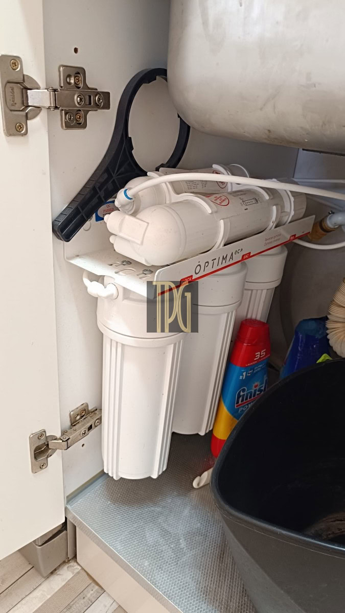 Under-sink water filtration system with reverse osmosis filters inside a cabinet, with hoses and a drain line visible