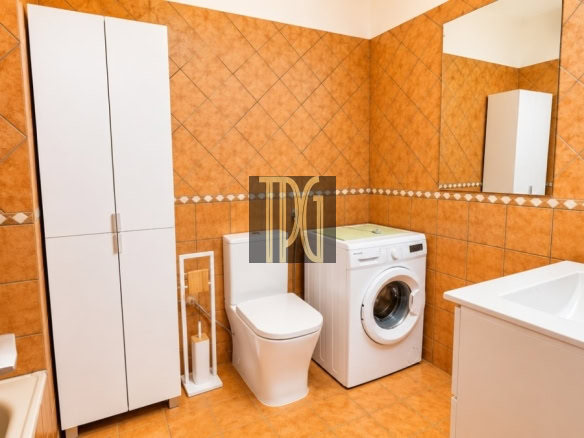 Bright orange-tiled bathroom with a tall white storage cabinet, toilet, front-loading washing machine, and a white sink with a mirror above it.