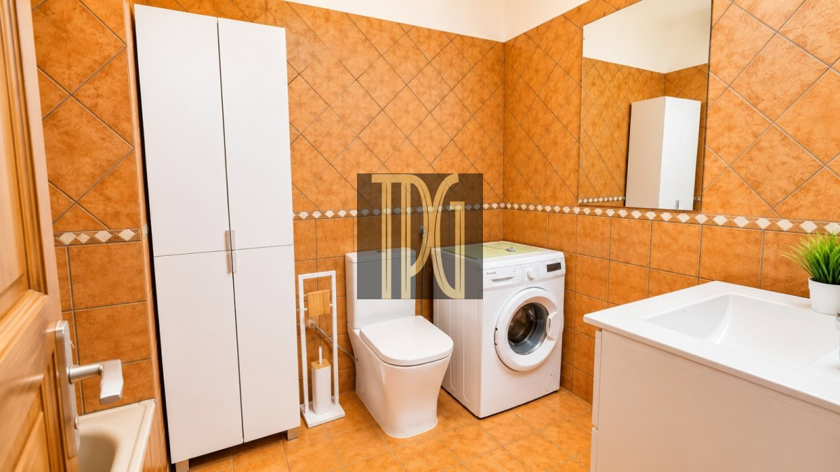 Bright orange-tiled bathroom with a tall white storage cabinet, toilet, front-loading washing machine, and a white sink with a mirror above it.