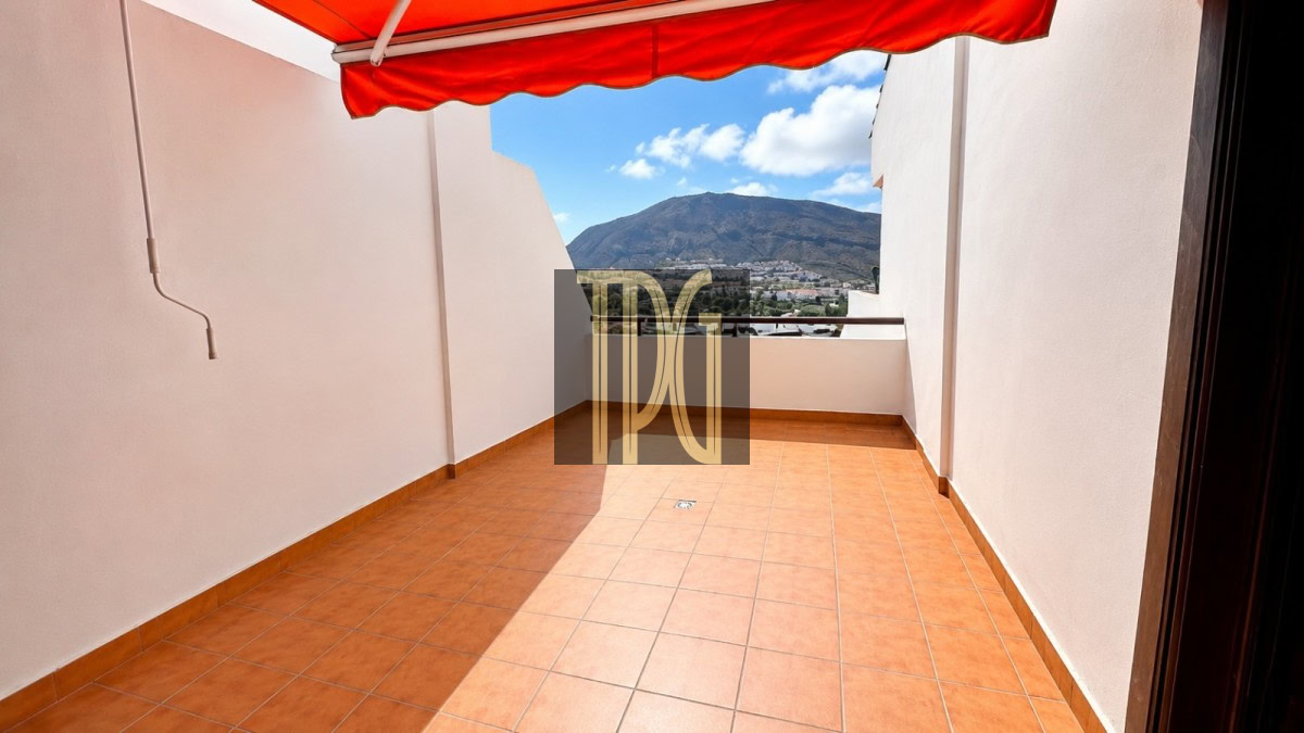 Terracotta-tiled rooftop terrace with a red awning and a mountain view behind white walls.