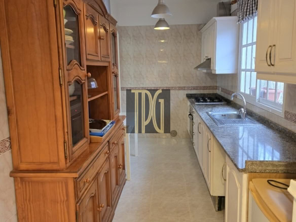 Narrow galley kitchen with a tall wooden cabinet on the left, white upper cabinets on the right, granite countertops, and three pendant lights overhead.
