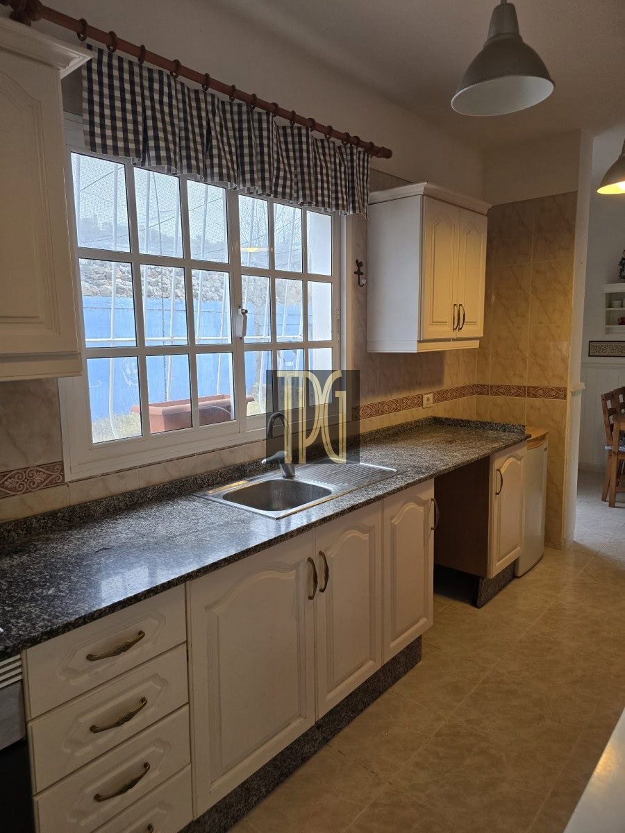Bright kitchen with white cabinets, granite countertop, and double sink under a large window with a blue-and-white checkered valance.