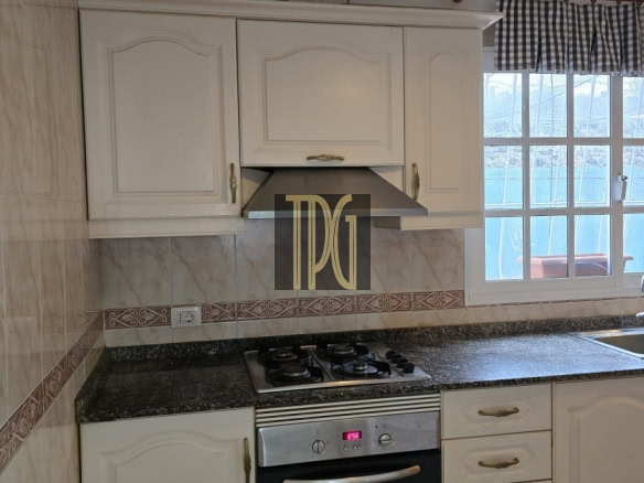 White kitchen cabinets above a granite countertop with a stainless steel gas range and oven, range hood, and a window to the right.
