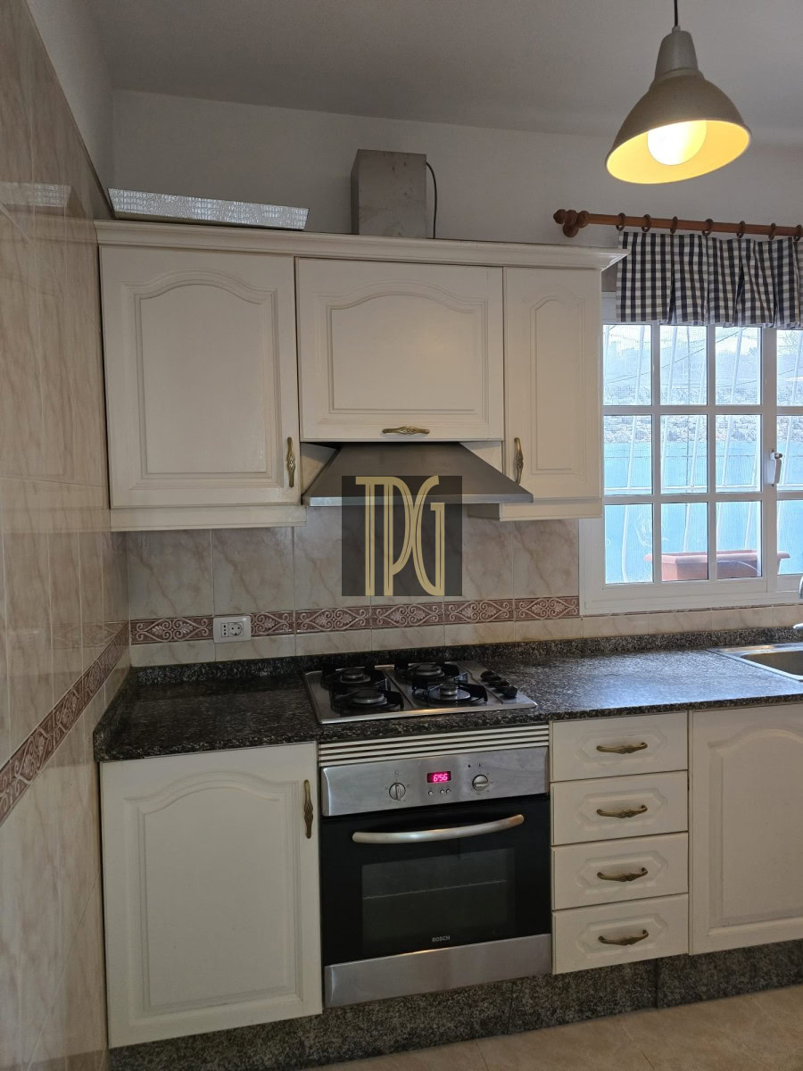 White kitchen cabinets above a granite countertop with a stainless steel gas range and oven, range hood, and a window to the right.