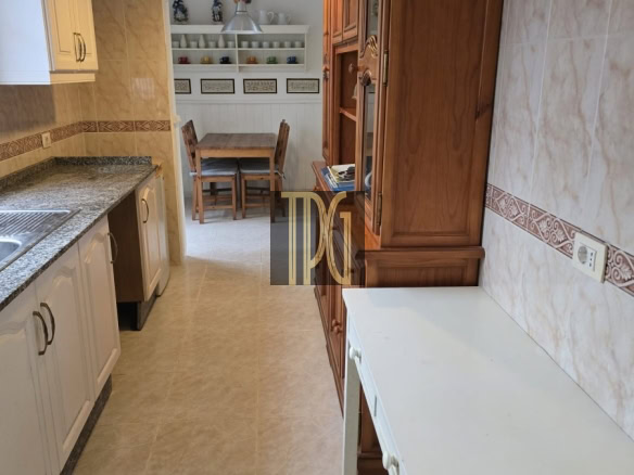 Kitchen with white cabinets, granite counter, and a wooden hutch; a small dining nook with a wooden table and chairs visible in the back.