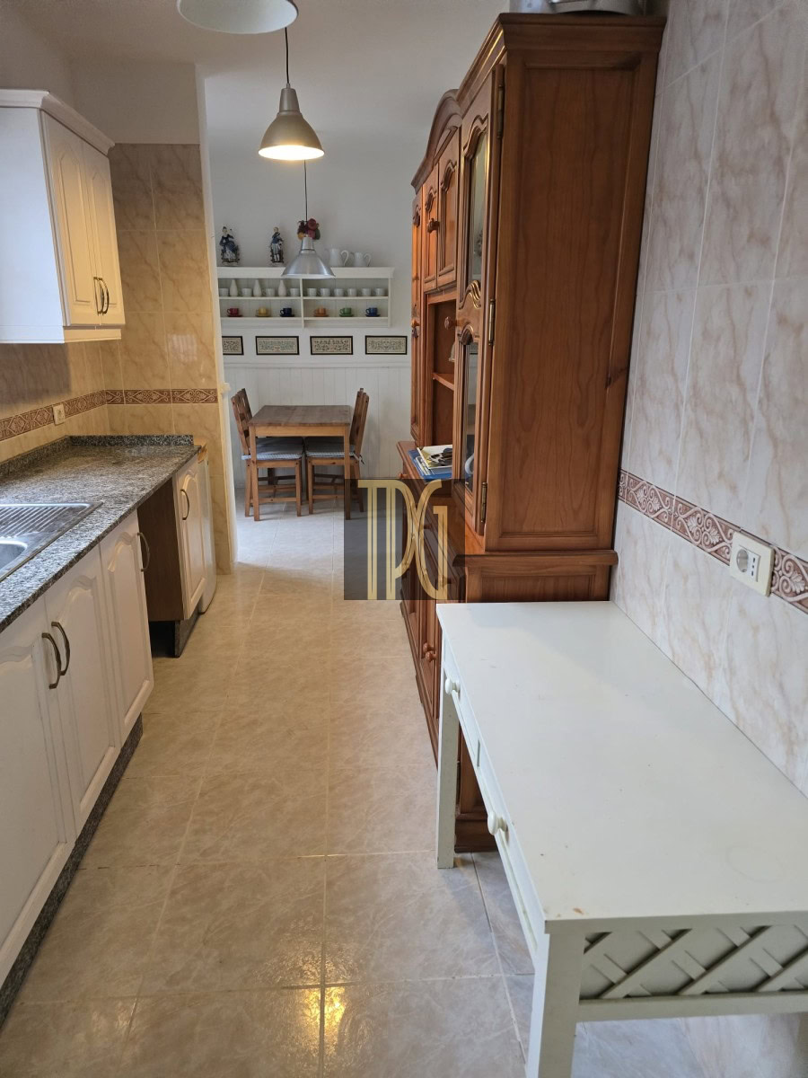 Kitchen with white cabinets, granite counter, and a wooden hutch; a small dining nook with a wooden table and chairs visible in the back.