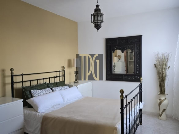 Bedroom with black metal bed frame, beige accent wall, white dressers, and a large ornate black mirror on the wall.