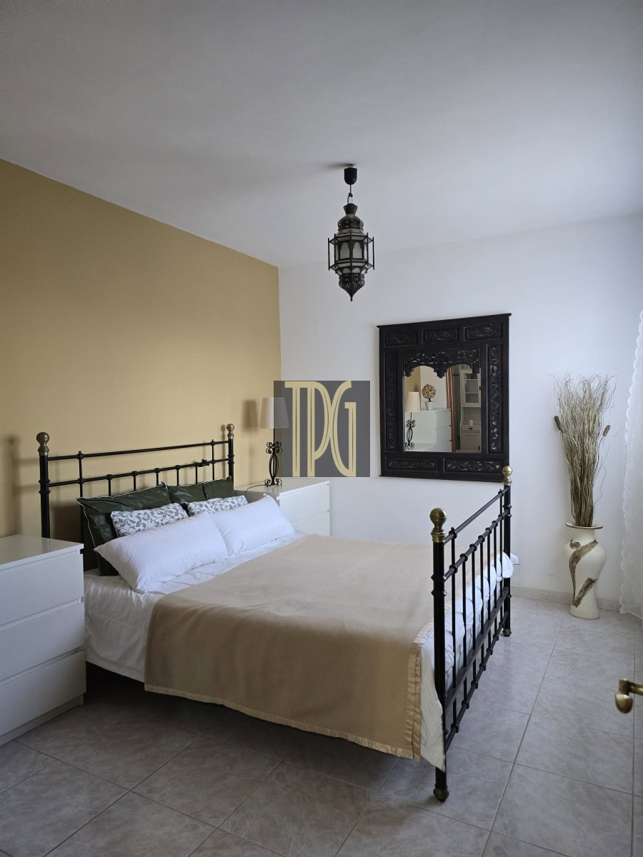 Bedroom with black metal bed frame, beige accent wall, white dressers, and a large ornate black mirror on the wall.