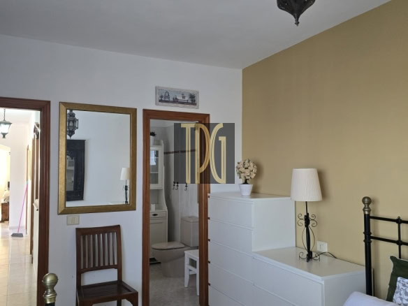 Bedroom with white dresser against a yellow wall, black metal bed frame, and a hanging lantern; bathroom doorway visible in the background.