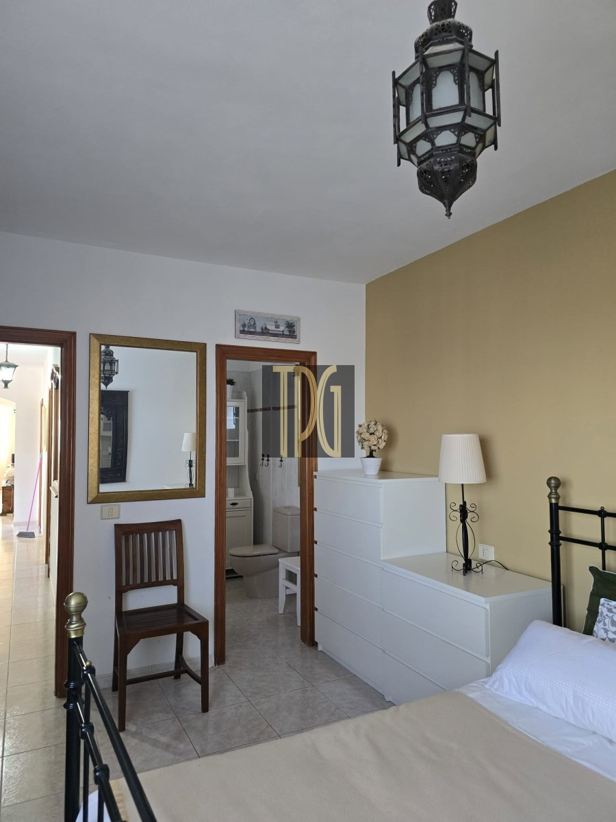 Bedroom with white dresser against a yellow wall, black metal bed frame, and a hanging lantern; bathroom doorway visible in the background.
