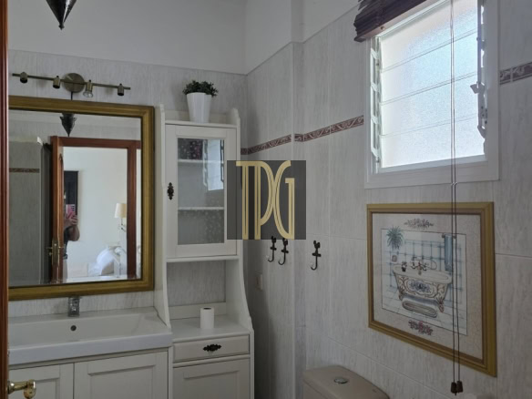 Bright white bathroom with vanity, mirror, and wall cabinet next to a toilet and small window with blinds