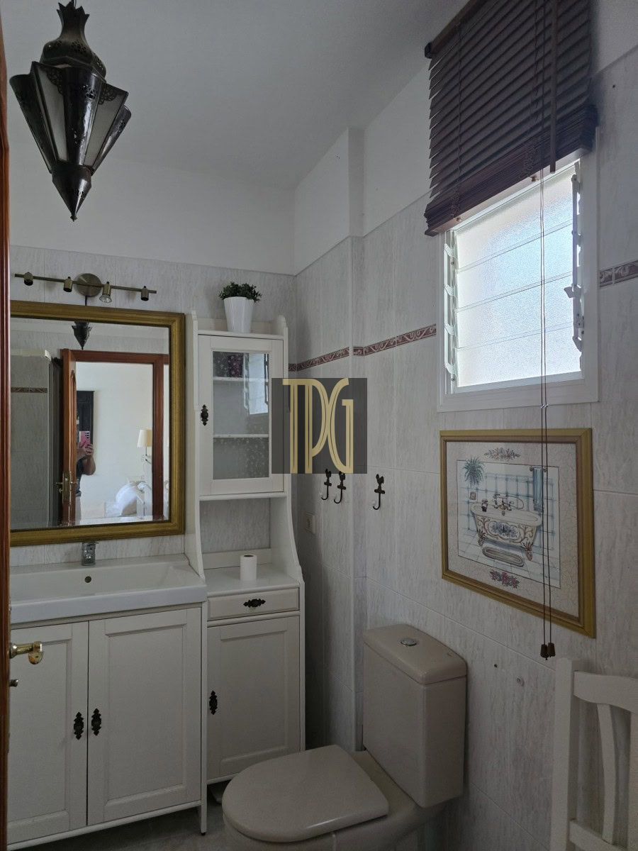 Bright white bathroom with vanity, mirror, and wall cabinet next to a toilet and small window with blinds
