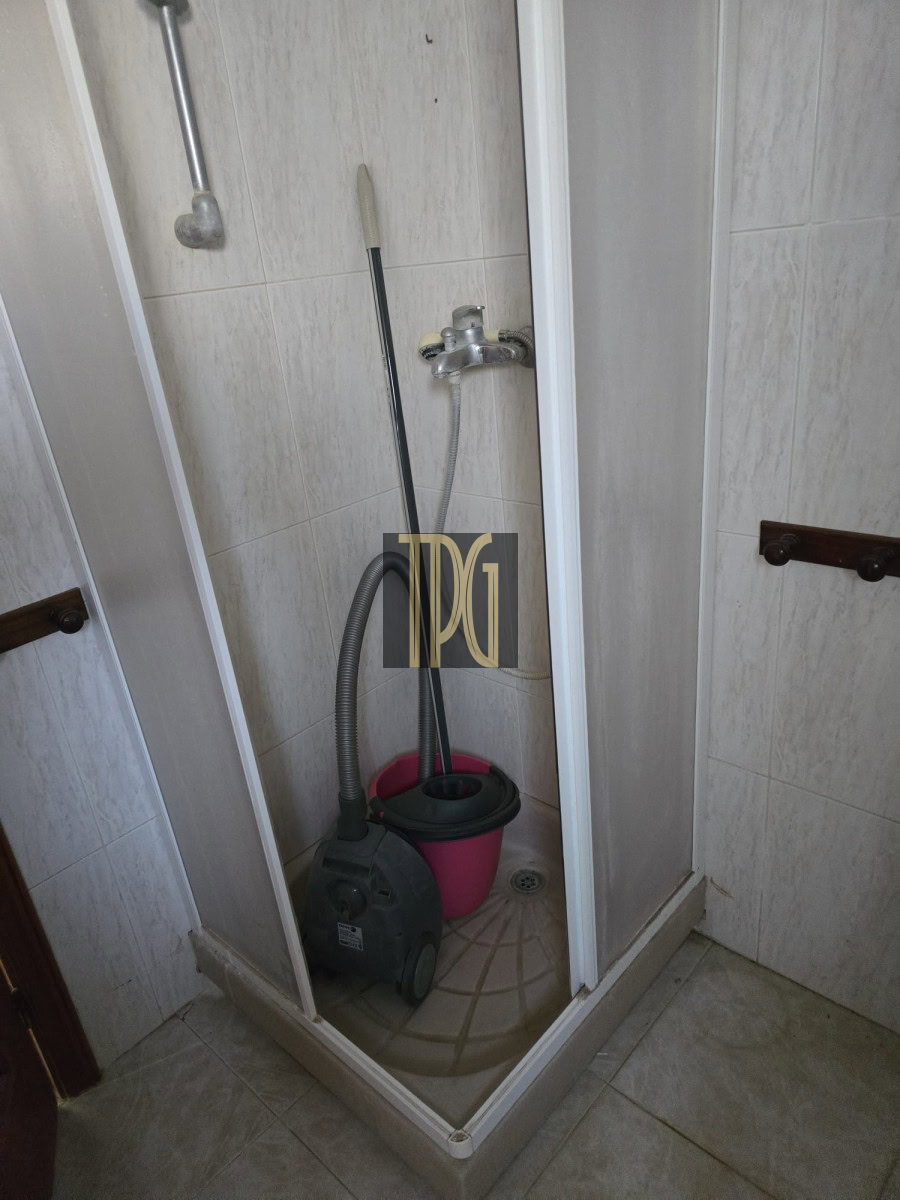 Shower stall containing cleaning supplies: a vacuum cleaner, pink bucket, and mop leaning inside the enclosure