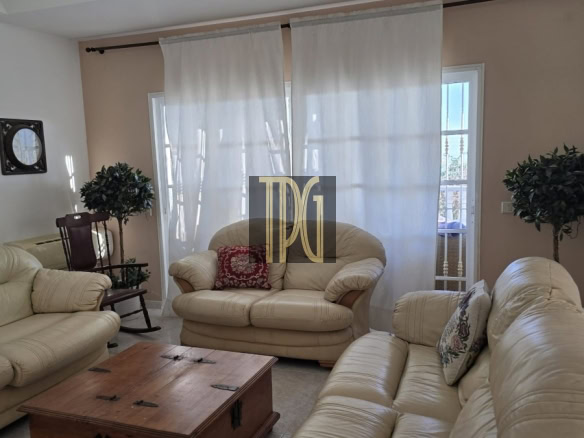 Beige leather living room with matching sofa set, a wooden trunk-style coffee table, and sheer white curtains with potted plants nearby.