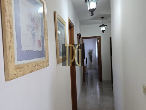 Narrow white-walled hallway with tiled floor, framed pictures on the left, and hanging lantern ceiling lights.
