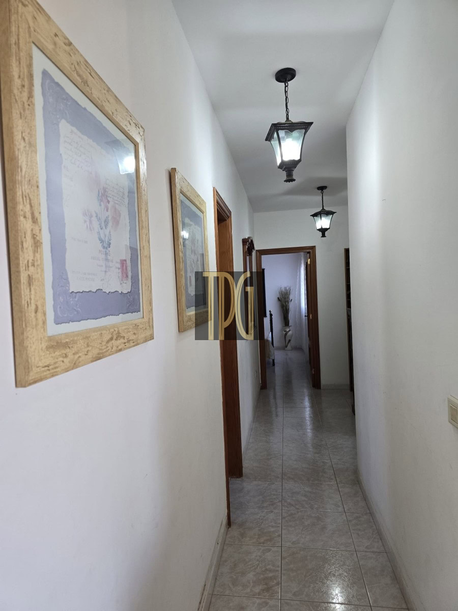 Narrow white-walled hallway with tiled floor, framed pictures on the left, and hanging lantern ceiling lights.